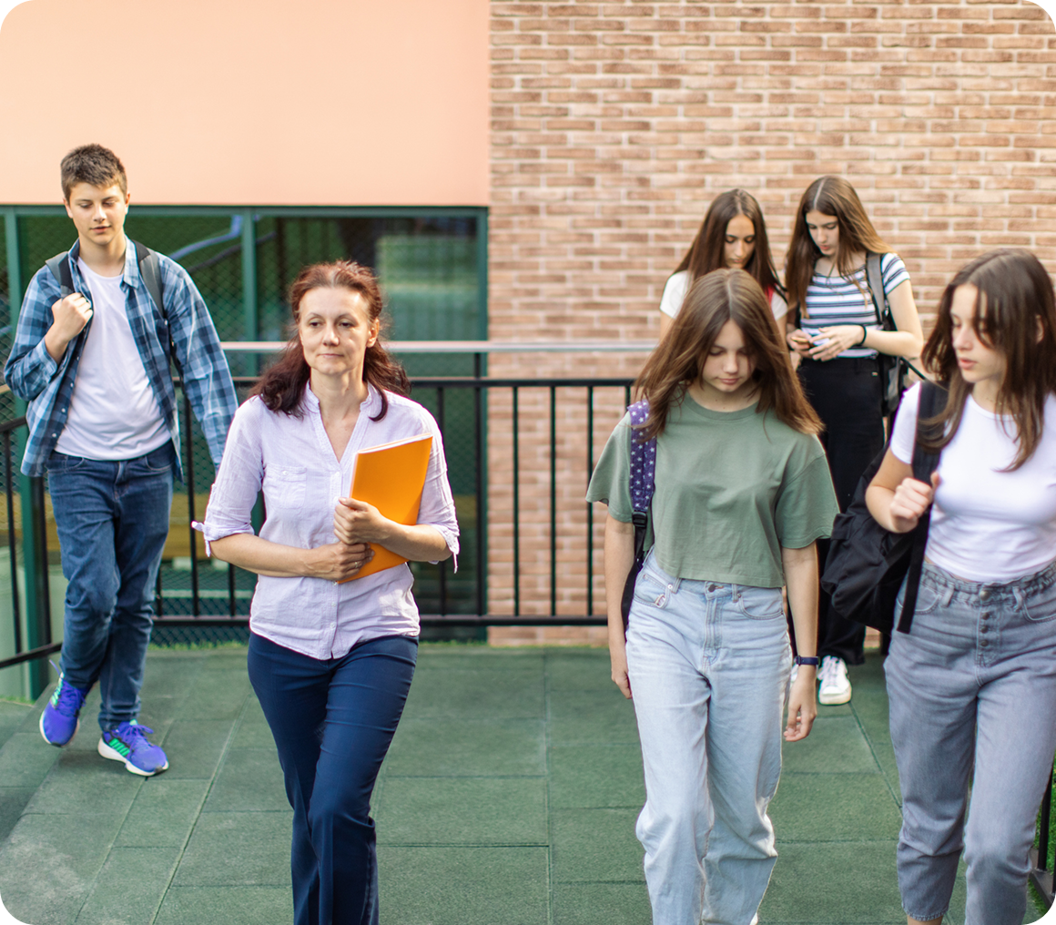 Teacher leading students outside school building.